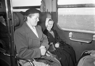 803823 Afbeelding van twee dames in een trein van de N.S., waarvan één in klederdracht.